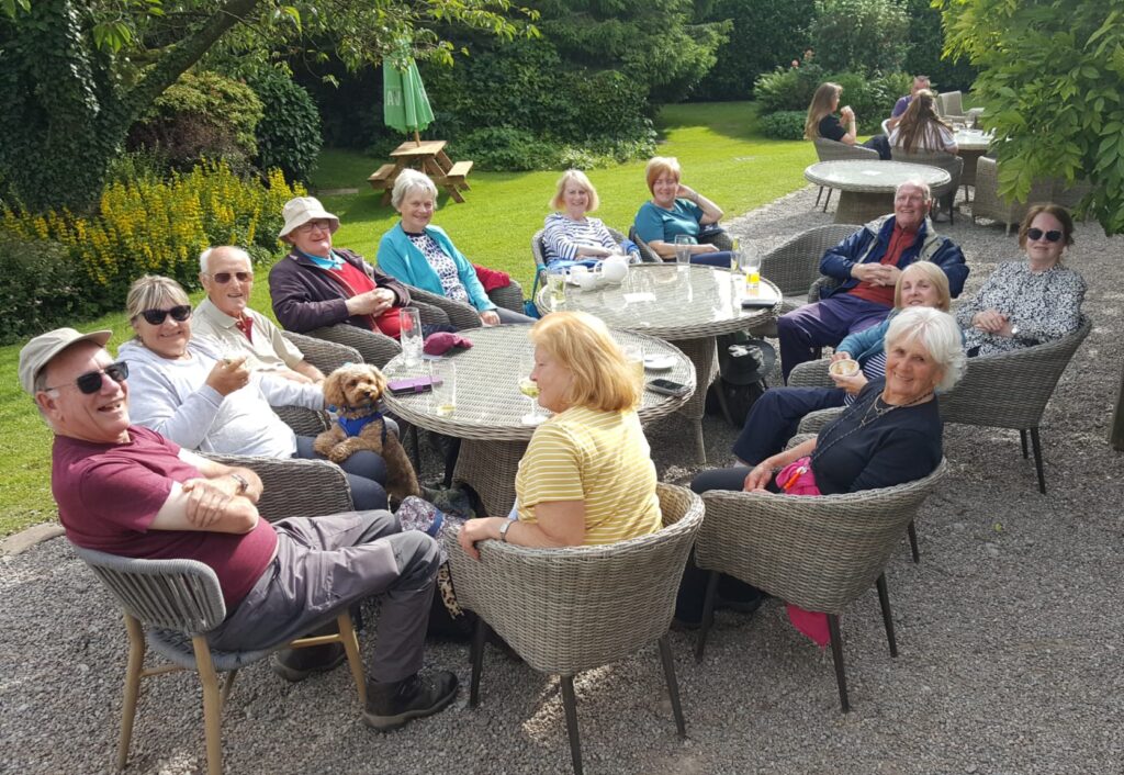 a grojup of members sitting around a table in the sunshine looking happy
